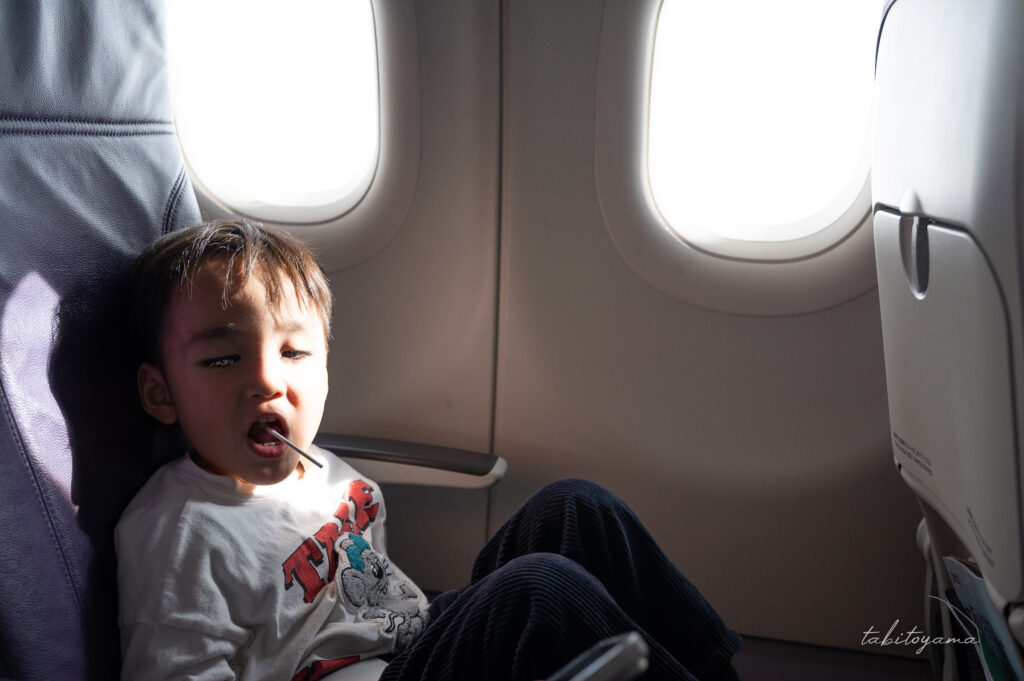 飛行機の窓際席で棒付きの飴を咥えながら余裕そうな表情の息子