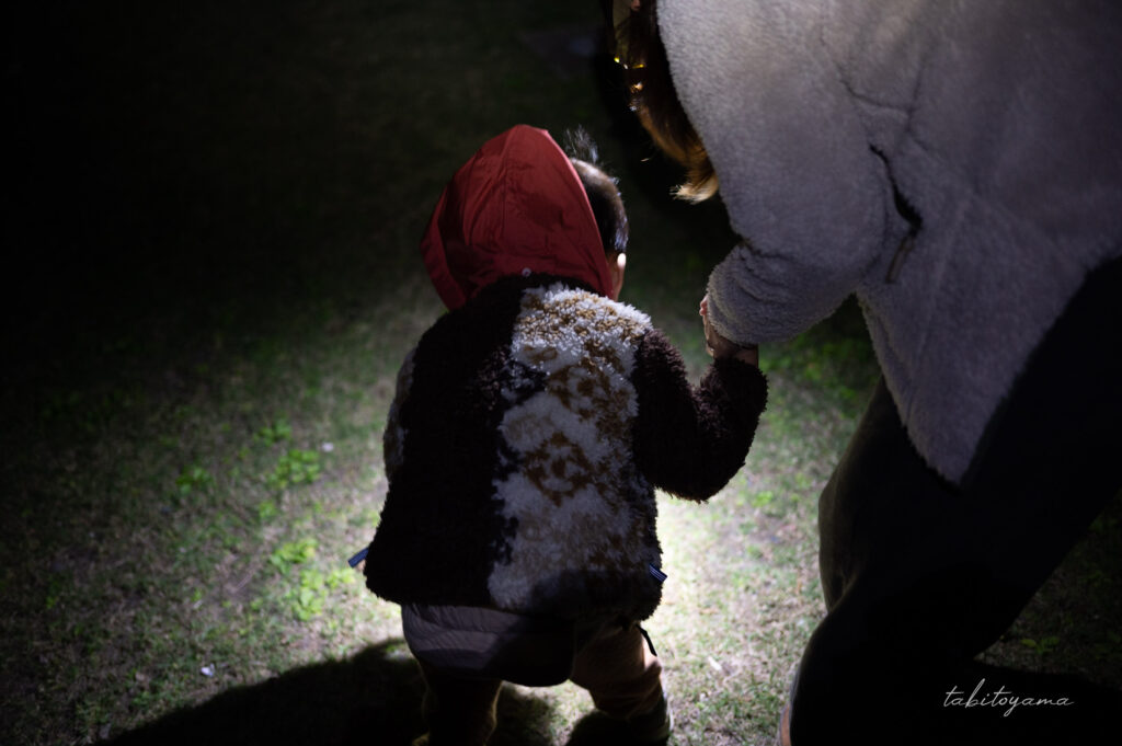 夜にヘッドライトに照らされた地面を眺める妻と息子