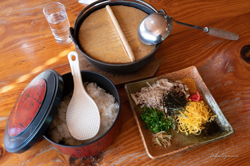 鉄鍋に入ったスープとおひつに入ったご飯と鶏飯の具材