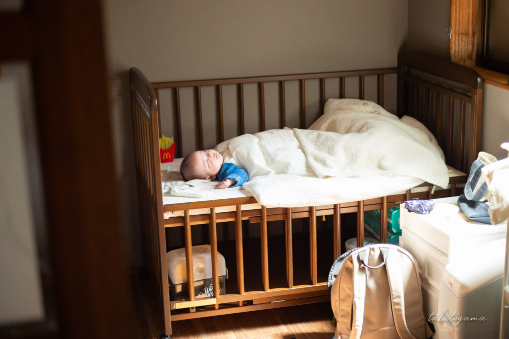 窓から光が注ぐベビーベッドに横たわる息子