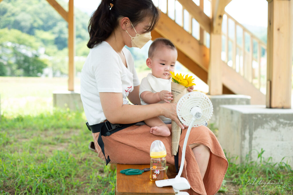 ひまわりを持ちながら扇風機で涼む妻と息子