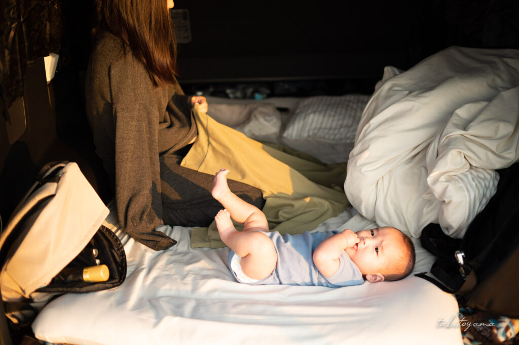 車内の敷いた布団で着替えようとする妻と寝転ぶ息子