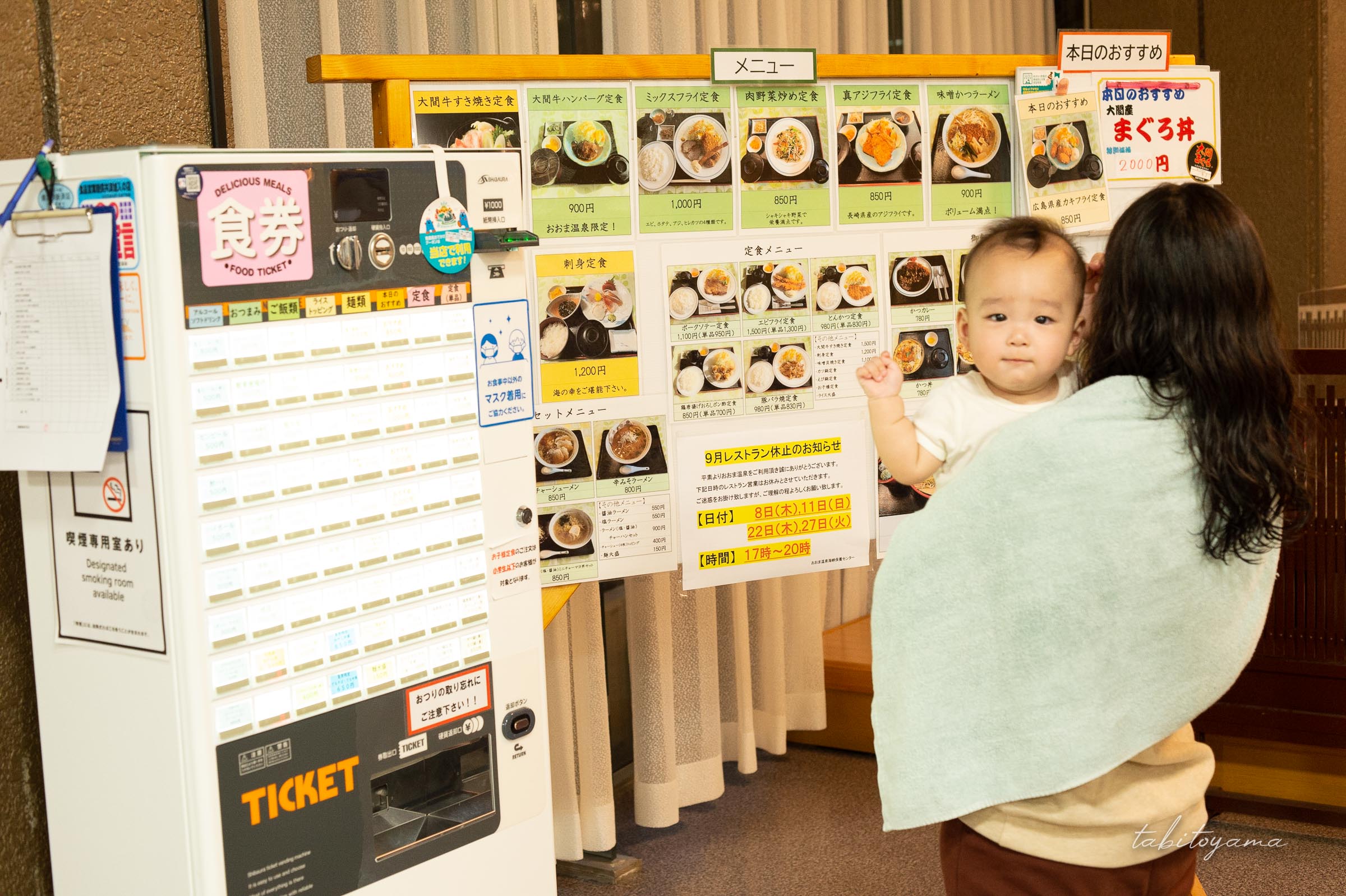 入浴施設に併設された食堂でメニューを見る後ろ姿の妻とカメラ目線の息子