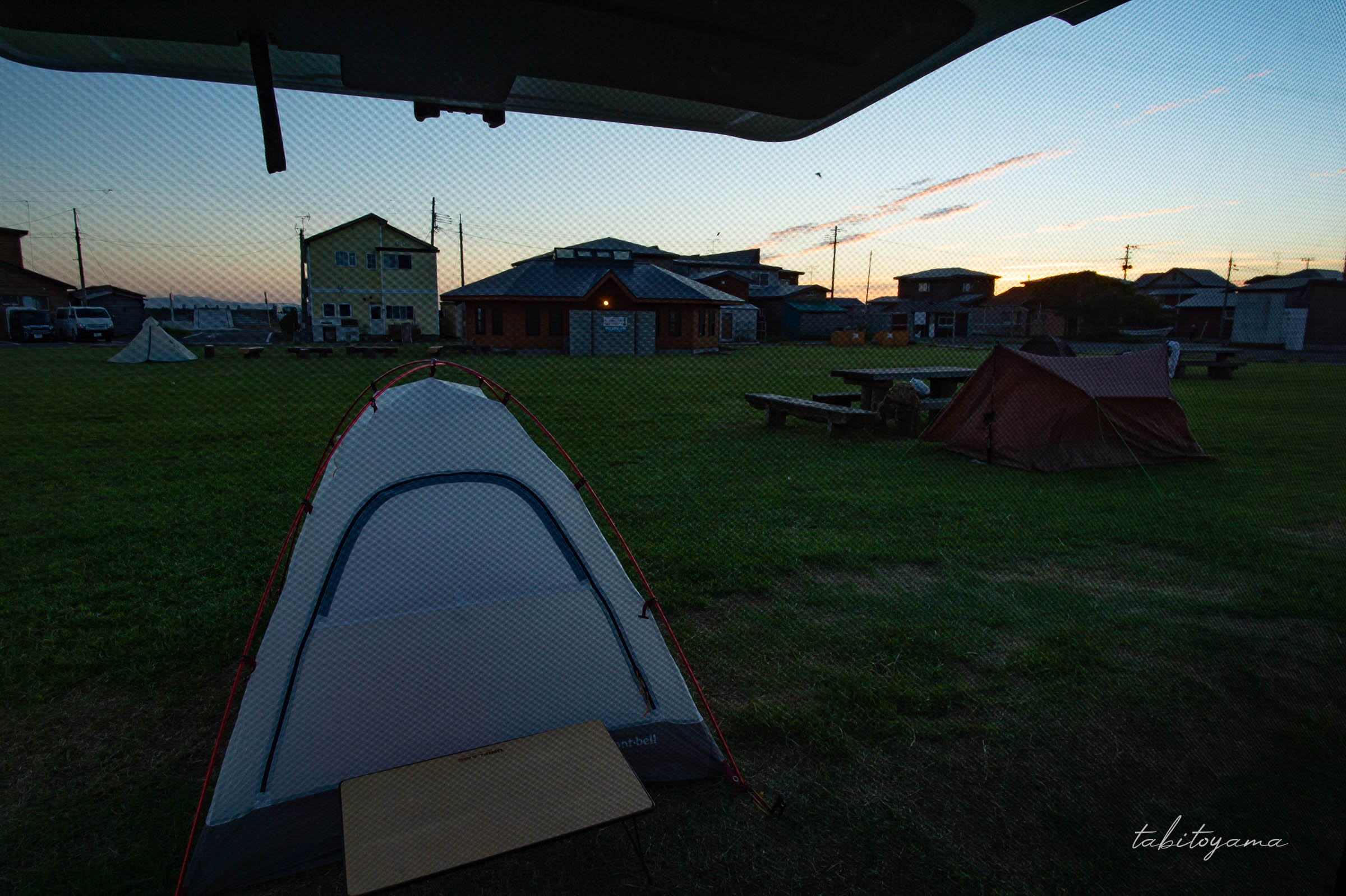 バックドアを開けた車内から見えるキャンプサイトとテントたち