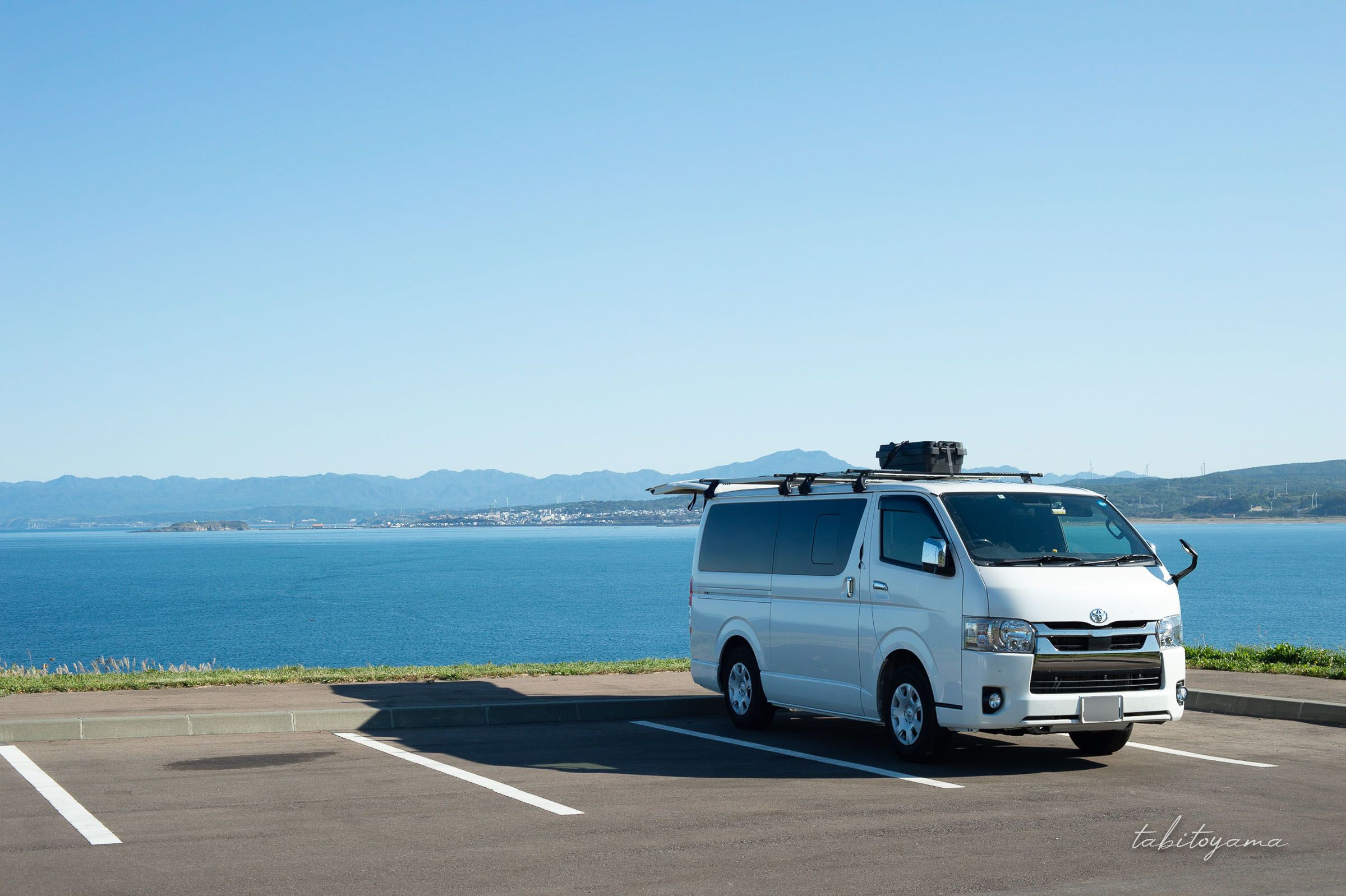 青い空と海を背景に駐車場に停まるハイエース