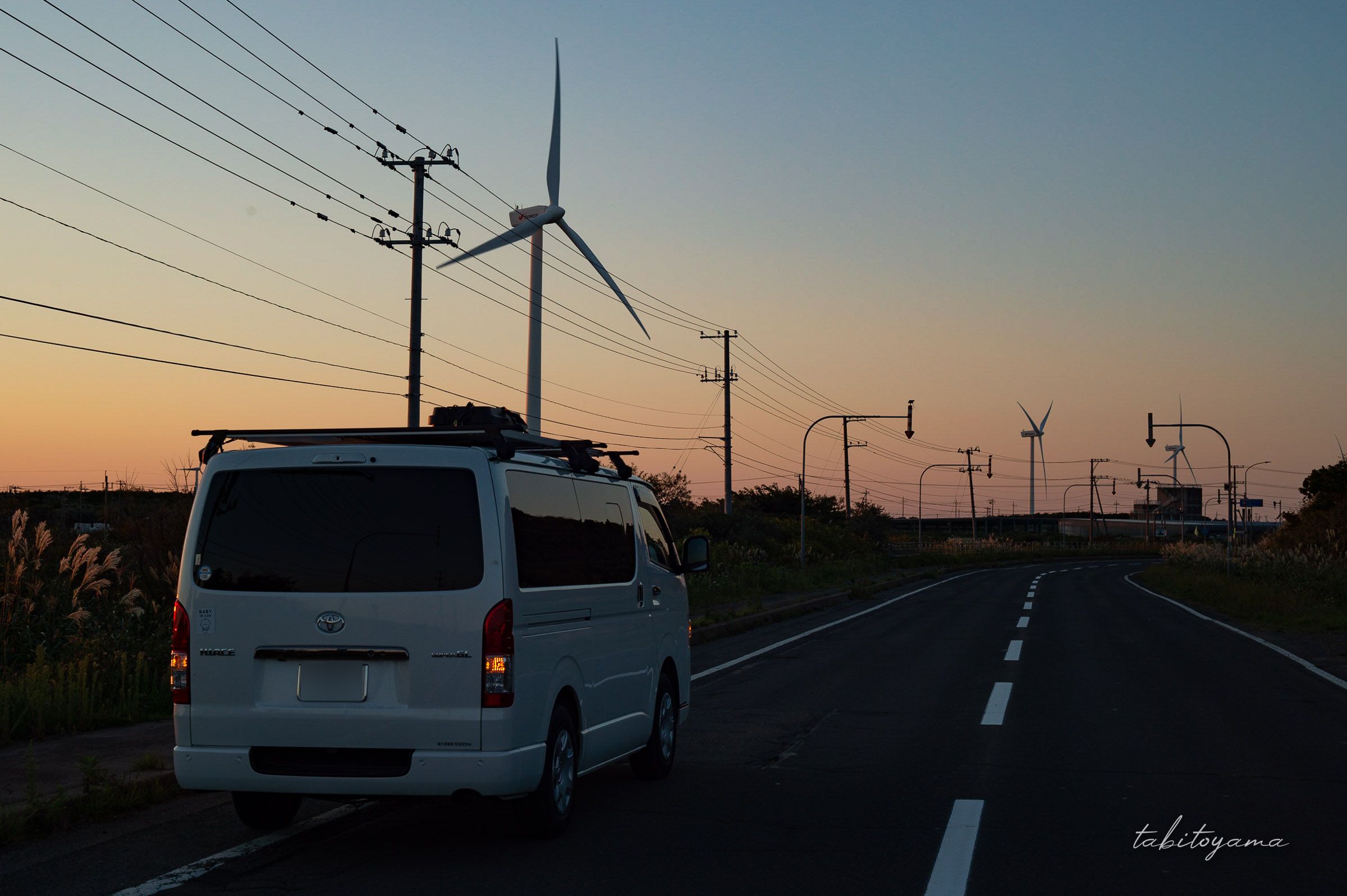 マジックアワーの空と風力発電が立ち並ぶ道路で停車するハイエース