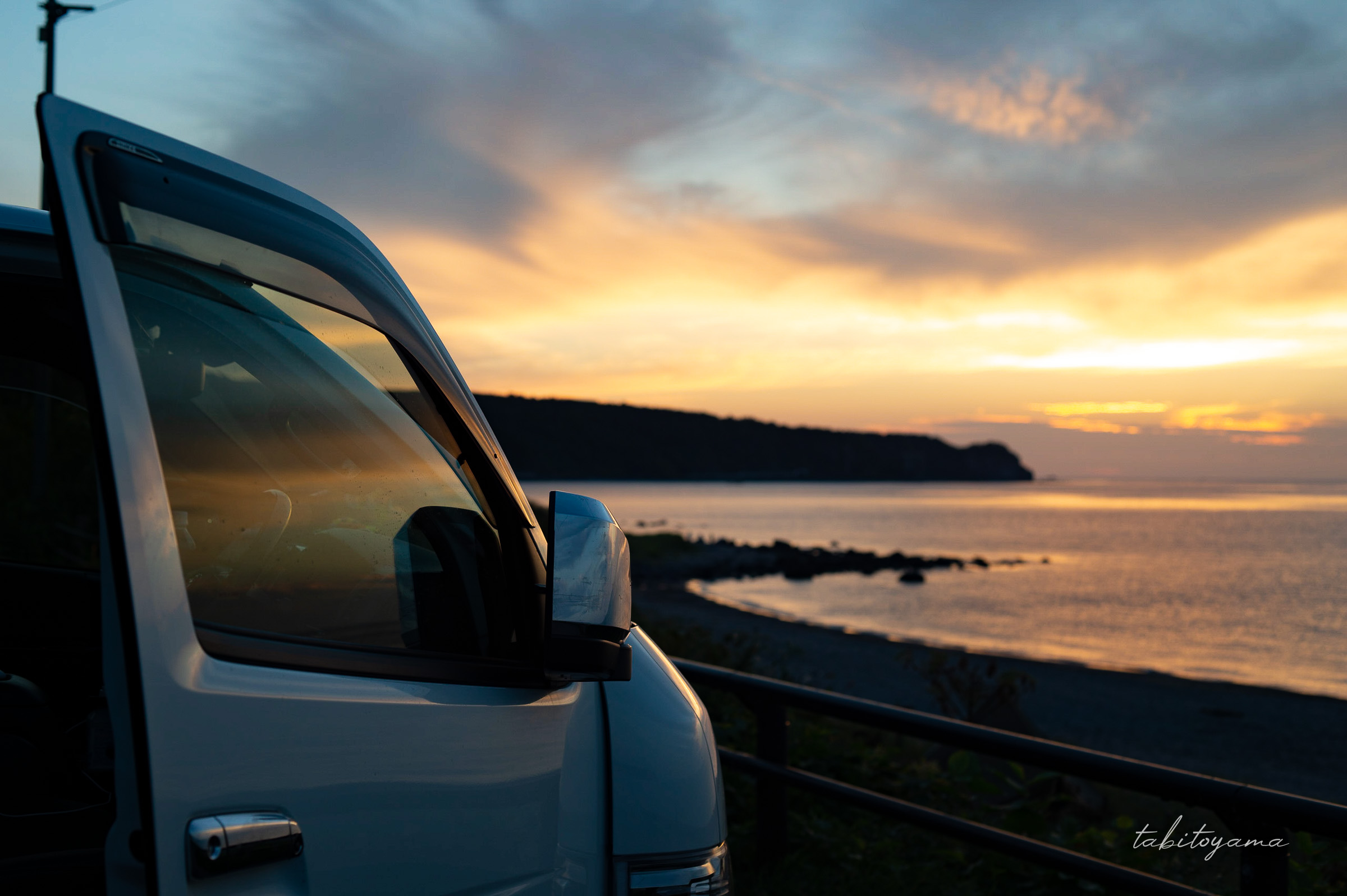 夕焼けに染まる空とその光が反射するハイエースの運転席のガラス