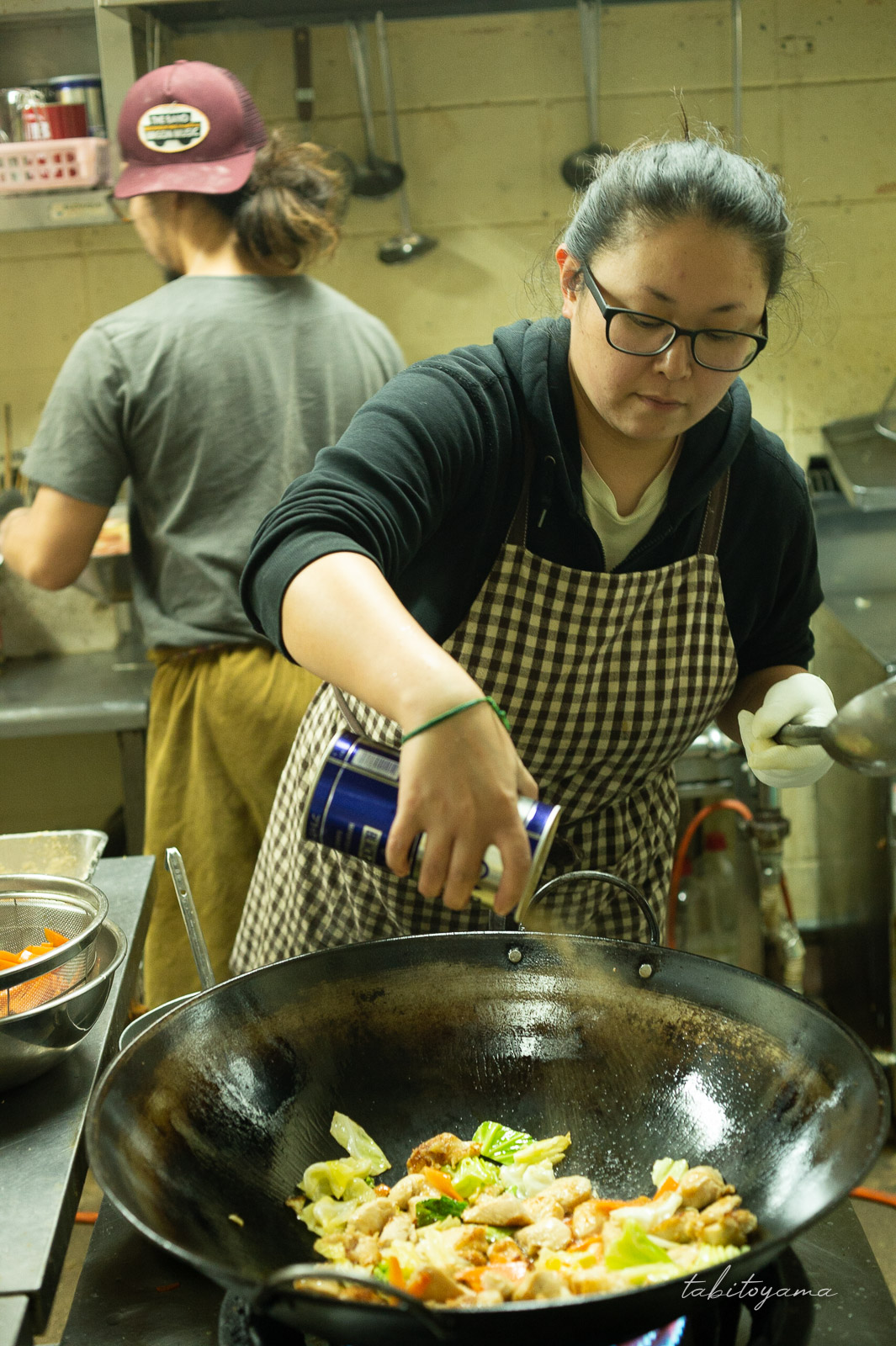 中華鍋に塩胡椒を振る小太りの女性と長髪男性の後ろ姿