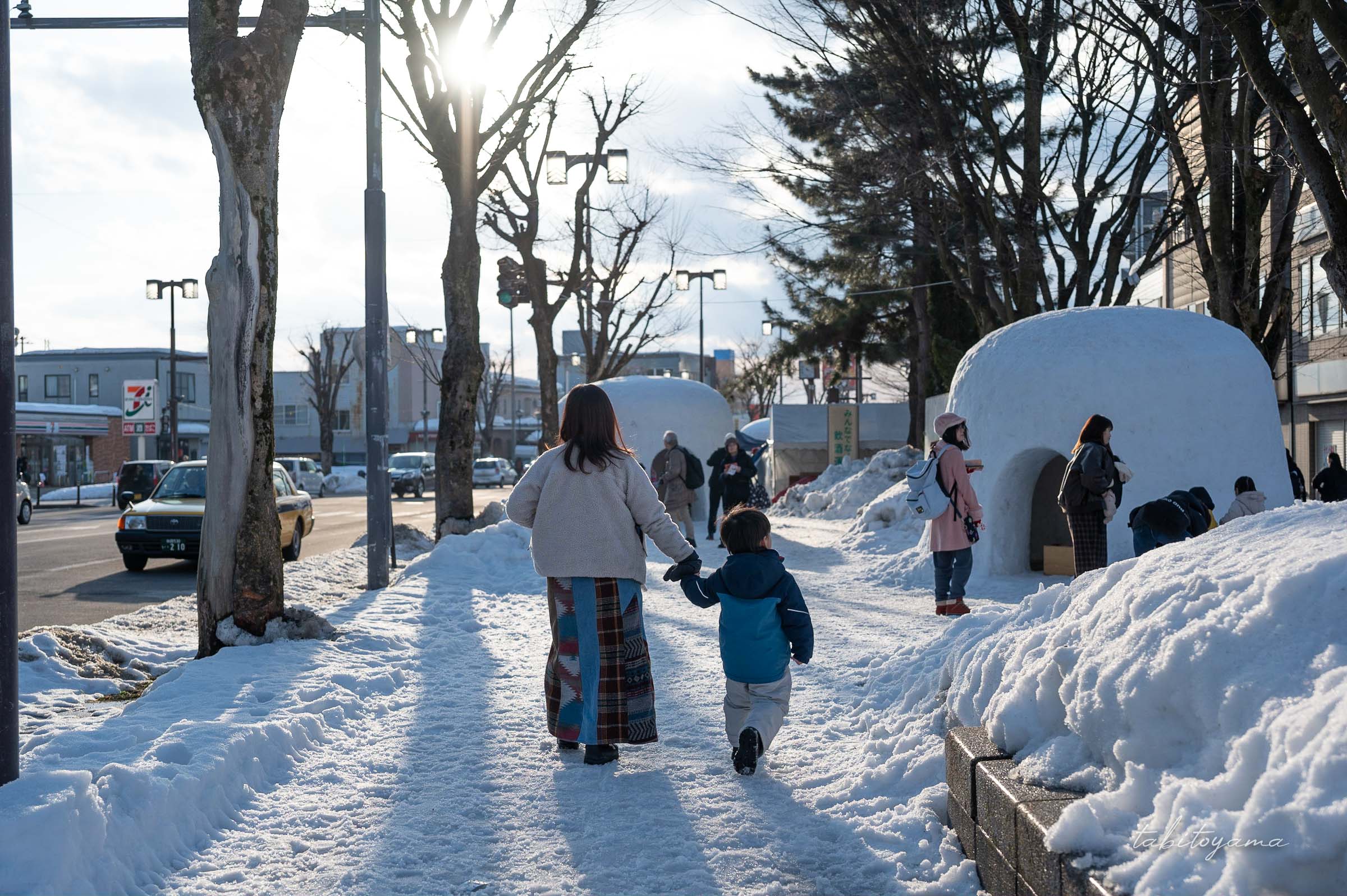 かまくらを横目に手を繋いで歩く妻と息子