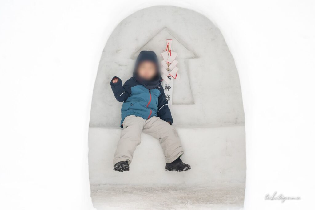 かまくらの中からカメラ目線で片手を上げる息子