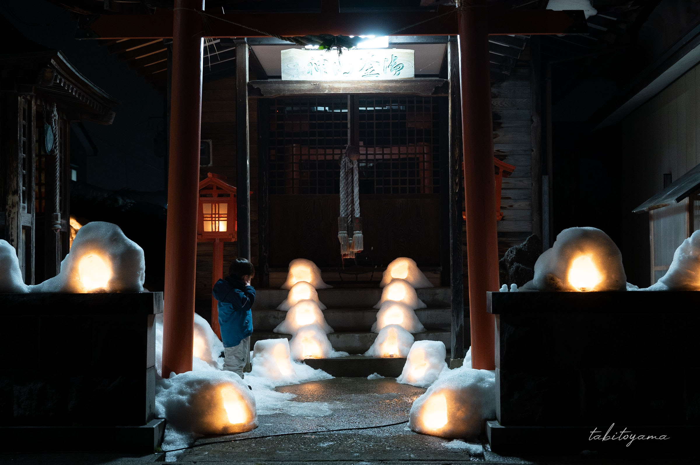 ミニかまくらが並べられた神社に佇む息子