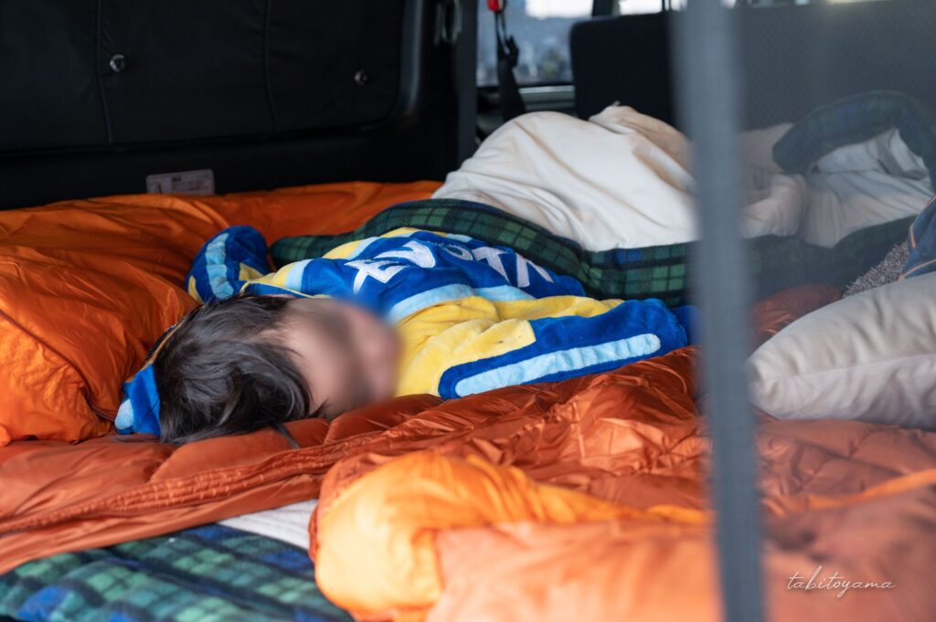 車中泊ベッドの上で寝袋に包まれて眠る息子