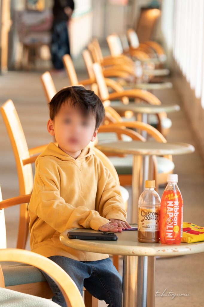 フェリーの窓際の席で折り紙をしながらこちらを向く息子