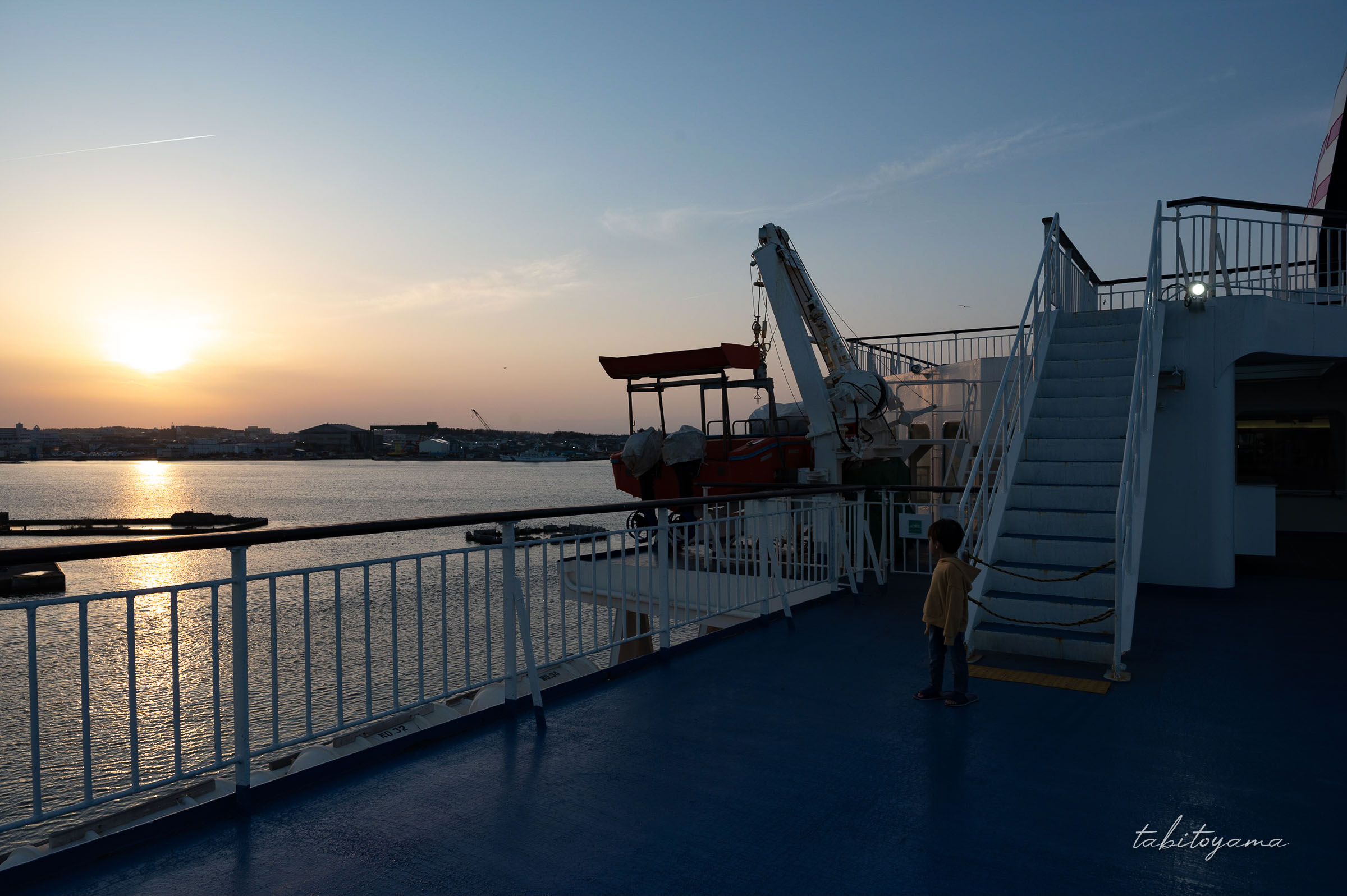 船上デッキで夕陽を眺める息子