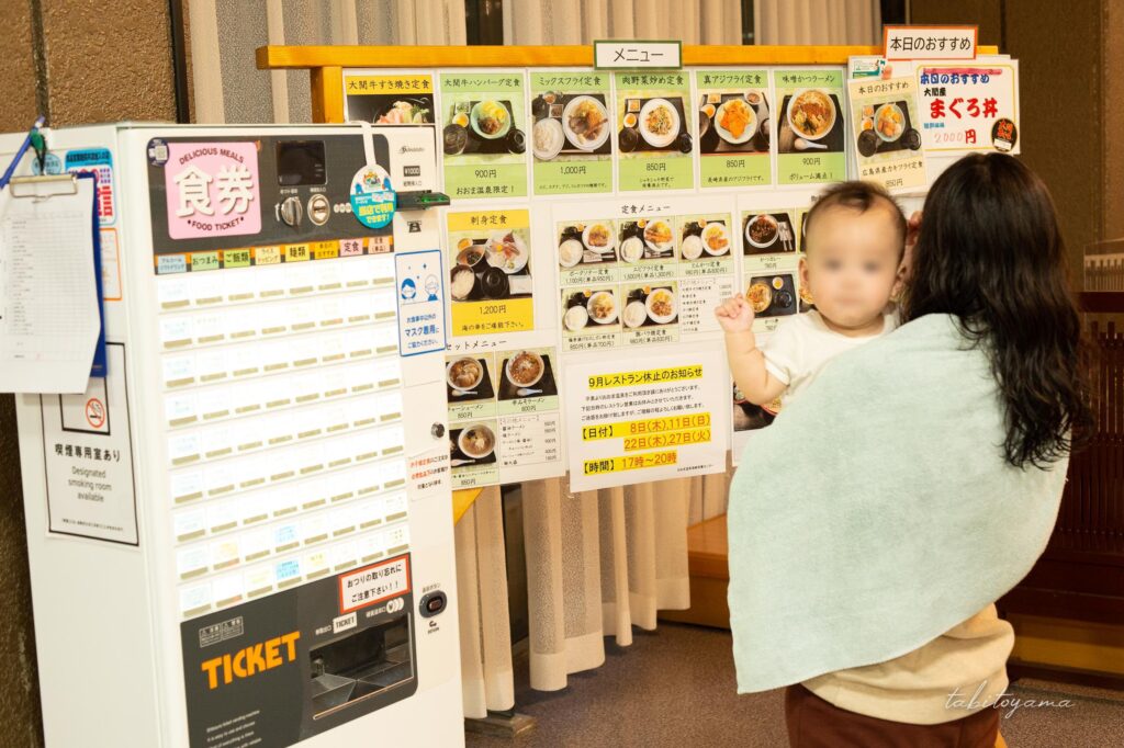 入浴施設に併設された食堂でメニューを見る後ろ姿の妻とカメラ目線の息子