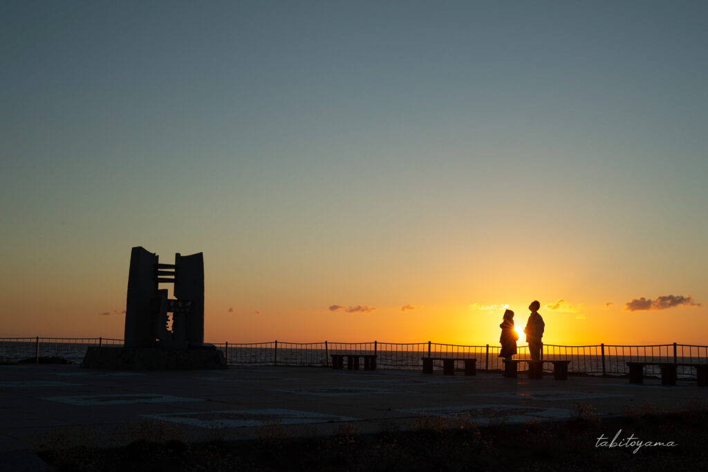 夕陽でシルエットになった黄金岬の波濤の門と二つの人影