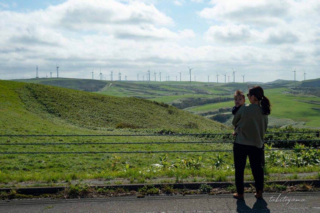 宗谷丘陵の道路から遠くに立ち並ぶ風車群を眺める妻と息子