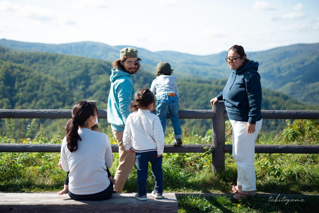 柵越しに山々を眺めながら談笑する妻と息子と友人家族