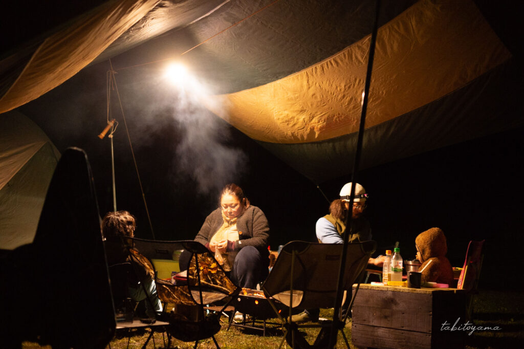 夜のキャンプ場でランタンの灯りの下で焚き火を囲む友人家族