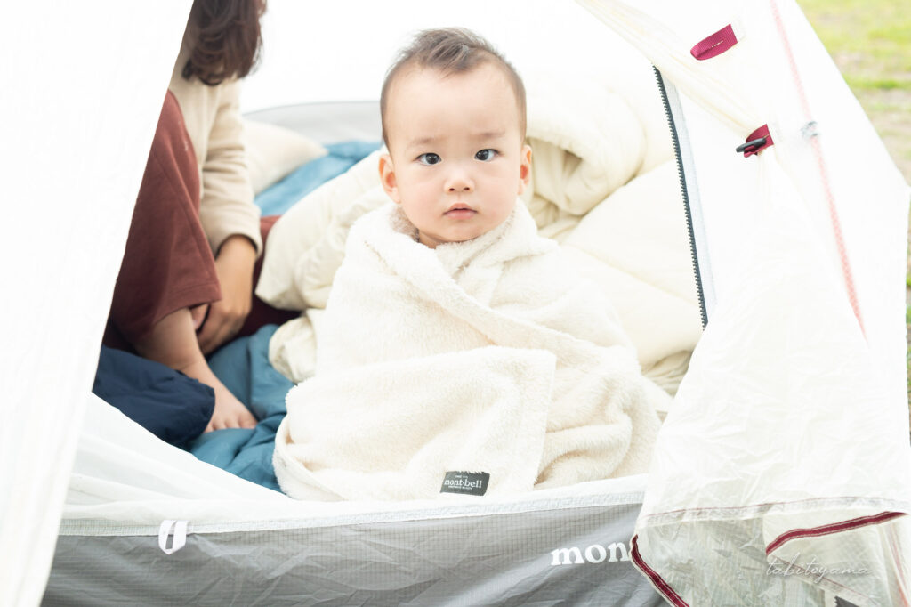 テントの出入り口でブランケットに包まる息子
