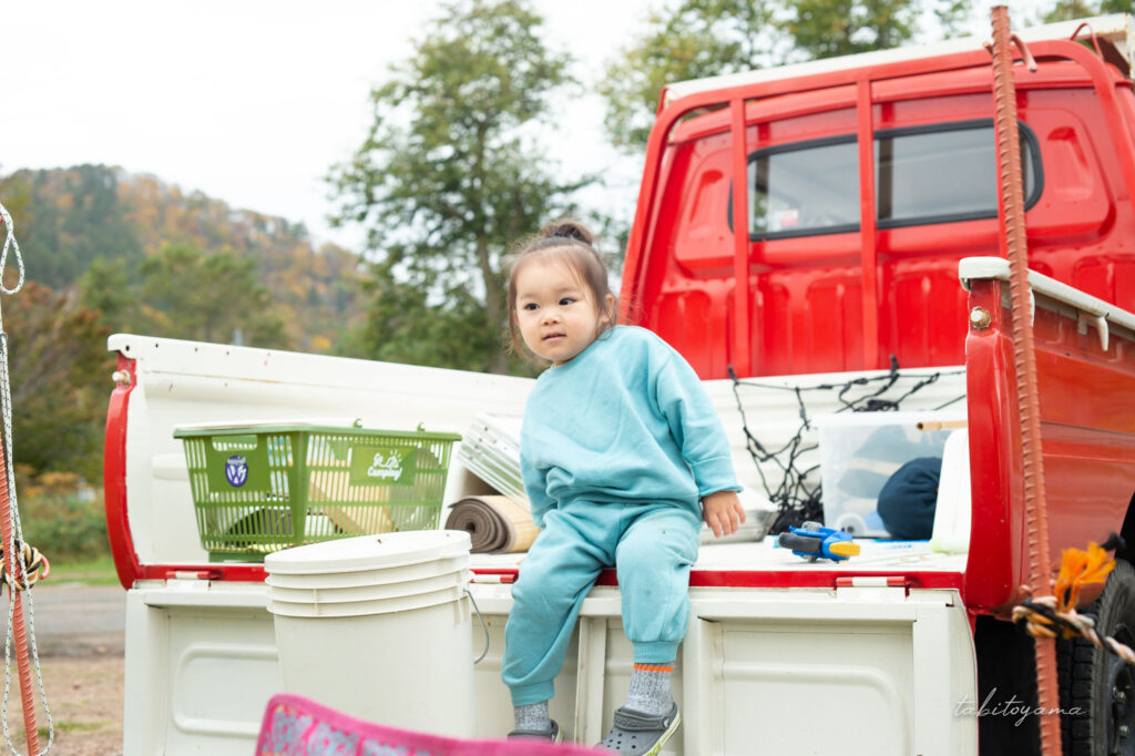 赤い日産ホーマーの荷台に腰掛ける友人の息子