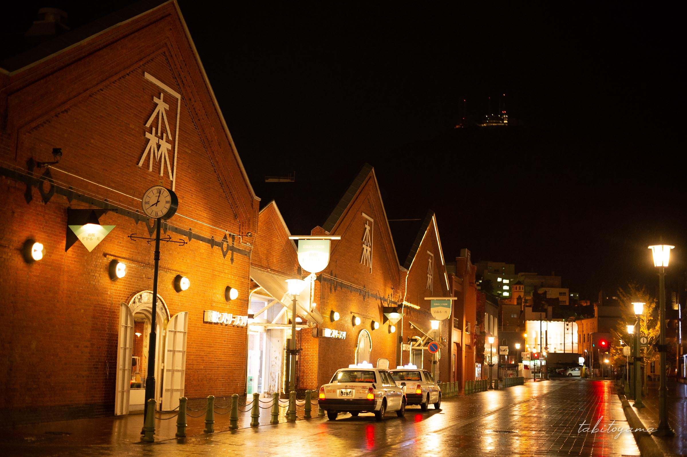 夜金森赤れんが倉庫軍前に停車するタクシー二台、街灯が濡れた路面に反射する
