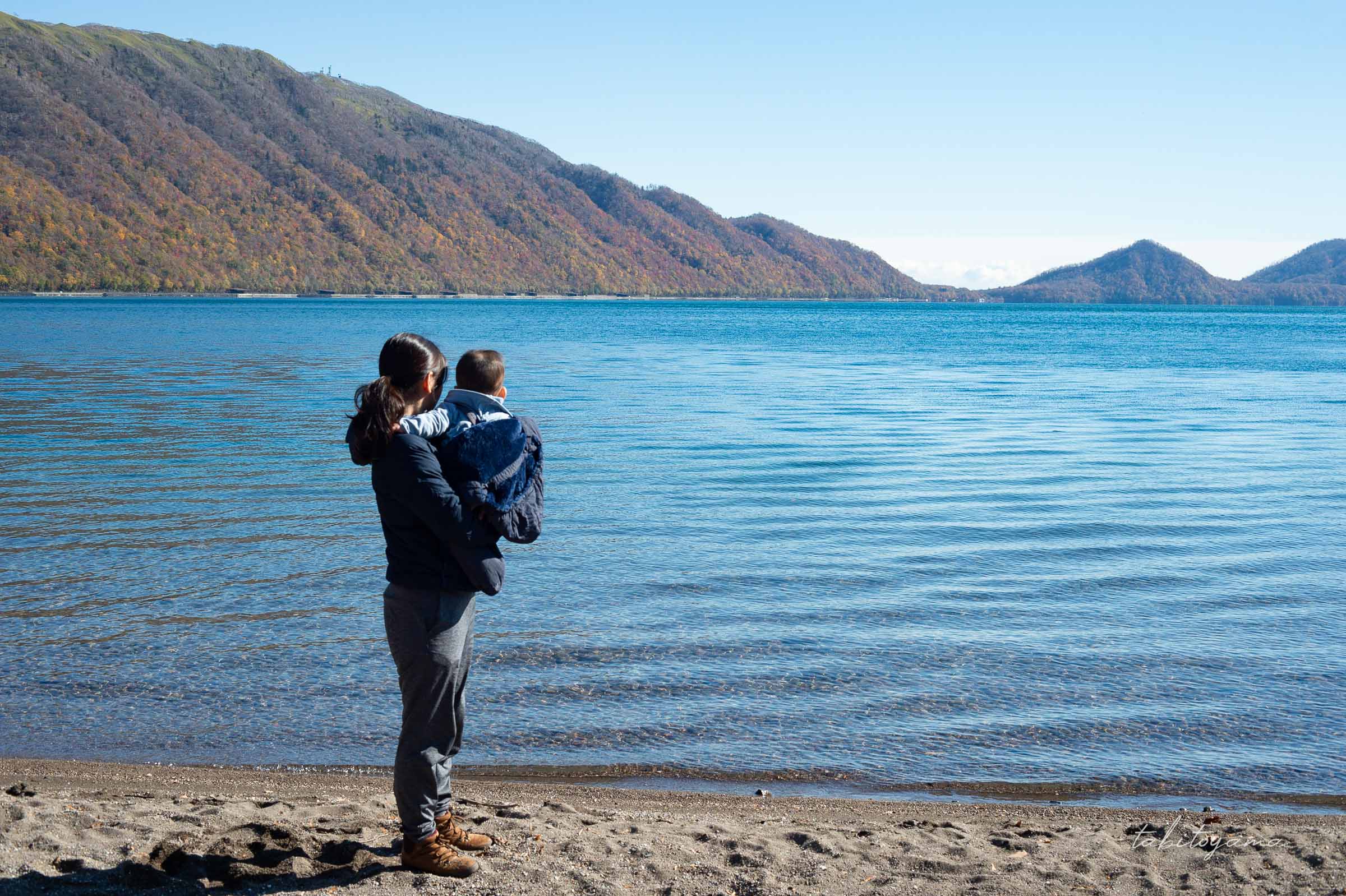 紅葉の山々と支笏湖、青い湖面を眺める妻と息子の後ろ姿