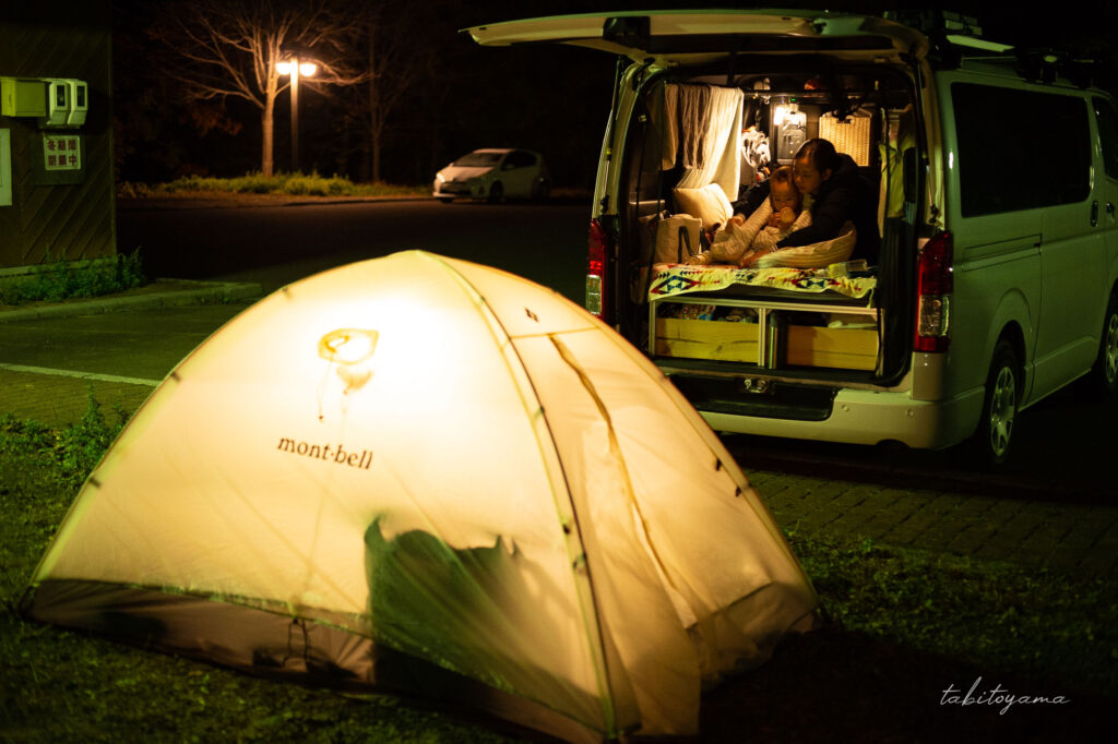 リアゲートを開けたハイエースの車内に妻と息子、そばにはランタンが灯るモンベルステラリッジテント