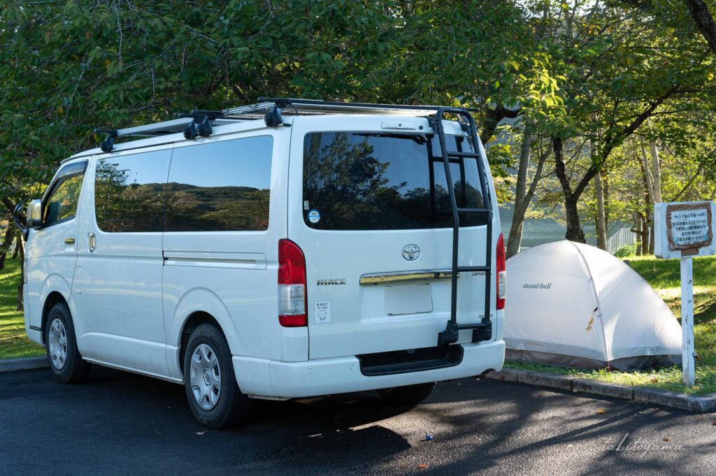 上磯ダム公園キャンプ場の駐車場で車中泊するハイエース。セミオートで白いテントが隣に設営されている。