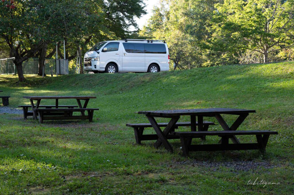 上磯ダム公園キャンプ場のフリーサイトに設置されたテーブルとベンチ。すぐそばには駐車場に停まるハイエース。