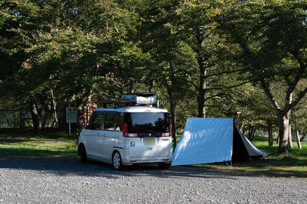 上磯ダム公園キャンプ場の駐車場に停まる軽自動車。横付けでタープが設営されている。