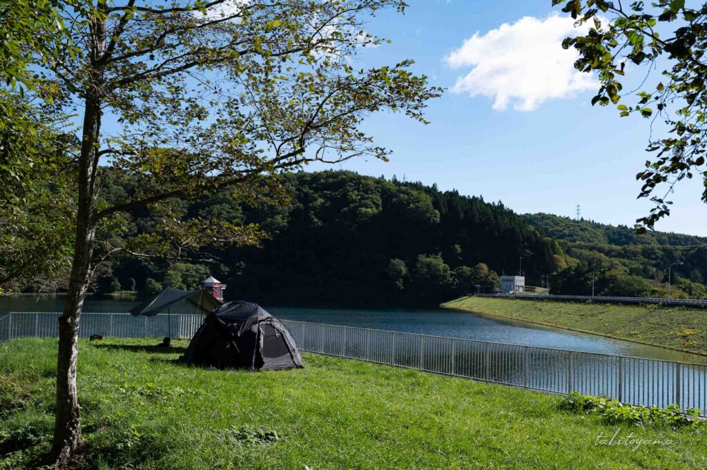 上磯ダム公園キャンプ場のダム湖沿いに設営された黒いテントとタープ。