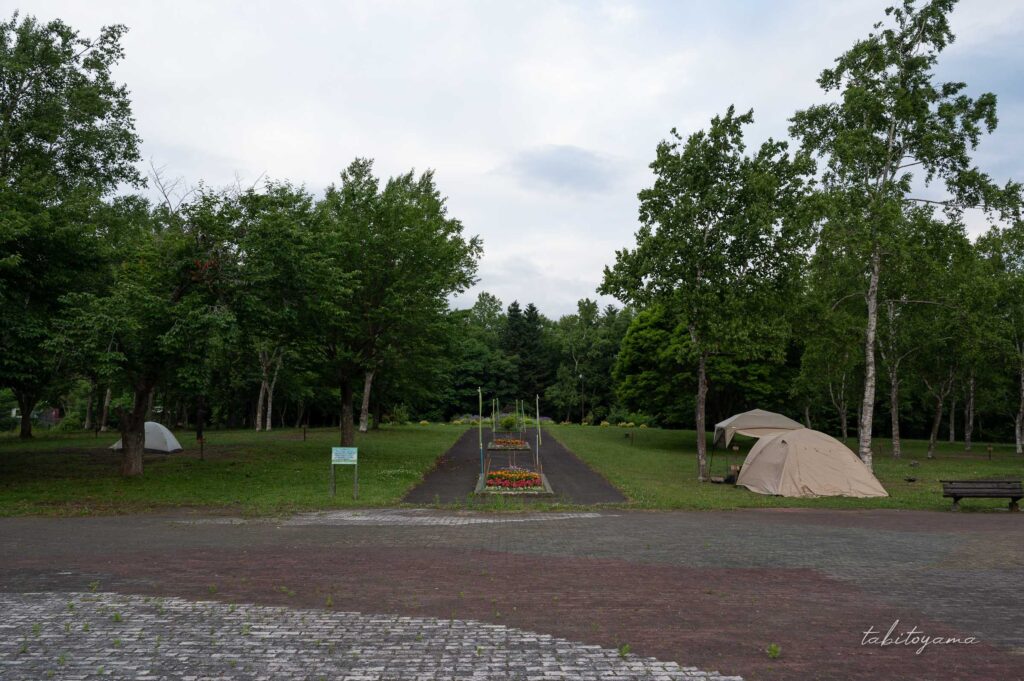 柏木地区レクリエーション施設の催し物広場からサイト全景を眺める。中央通路には花壇、両脇にはテントが設営されている。