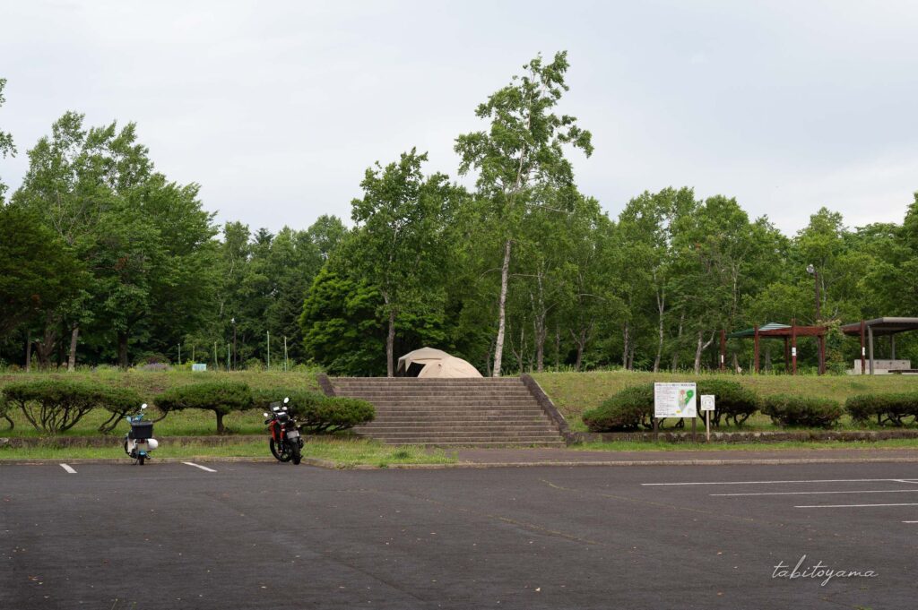 柏木地区レクリエーション施設の駐車場駐車するバイクが2台。奥の階段の先にはテントと炊事場が見える。