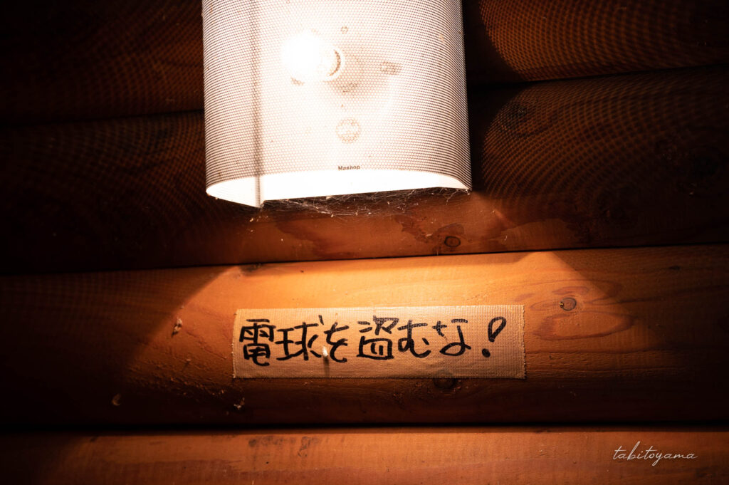 天塩川リバーサイドパークキャンプ場のトイレ内のライト。電球を盗むなとガムテープで注意書きが貼られている。