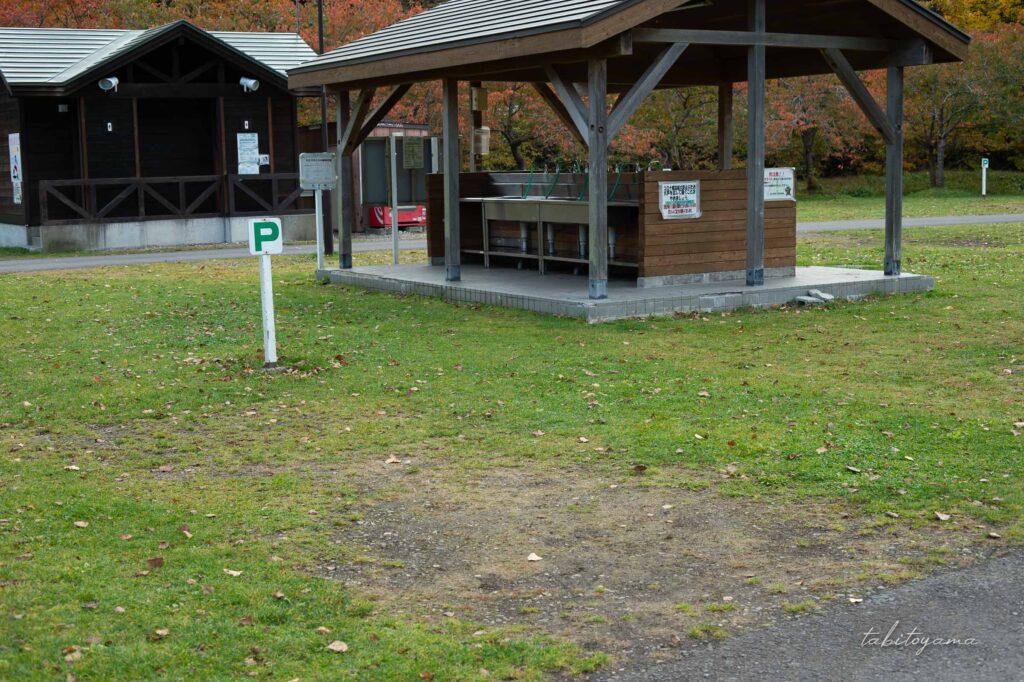 湯の沢水辺公園の炊事棟に隣接したオートサイト。奥にはトイレが見える。