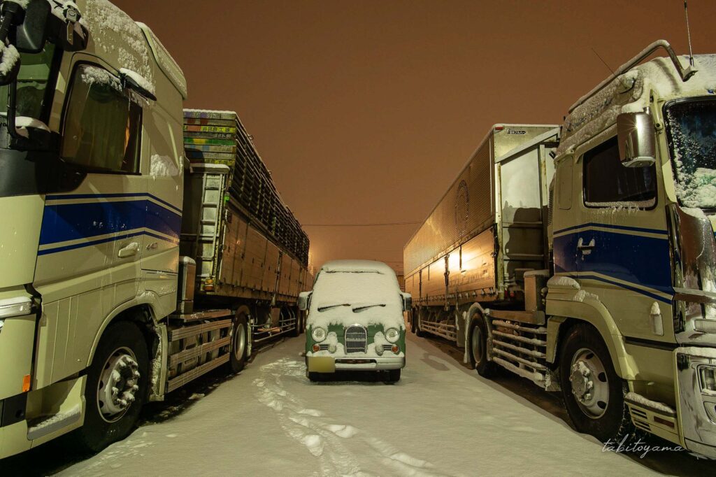 大型トラックに囲まれてフロントガラスに雪が積もったサンバーディアスクラシック