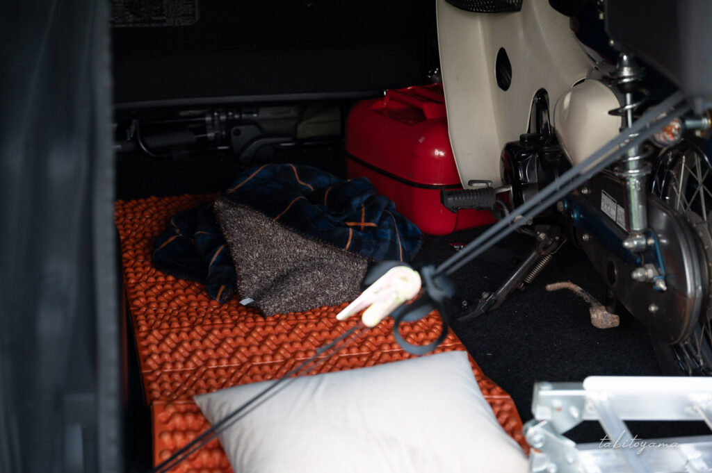 ハイエースの荷室に積載されたリトルカブのすぐ隣には、折り畳みマットや枕、ブランケットが置かれている
