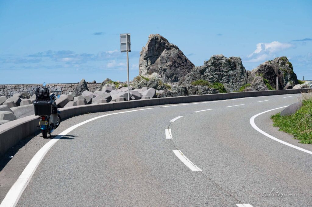 佐渡ヶ島の海沿いの道路に停車するリトルカブ、カーブの先には岩場が見える