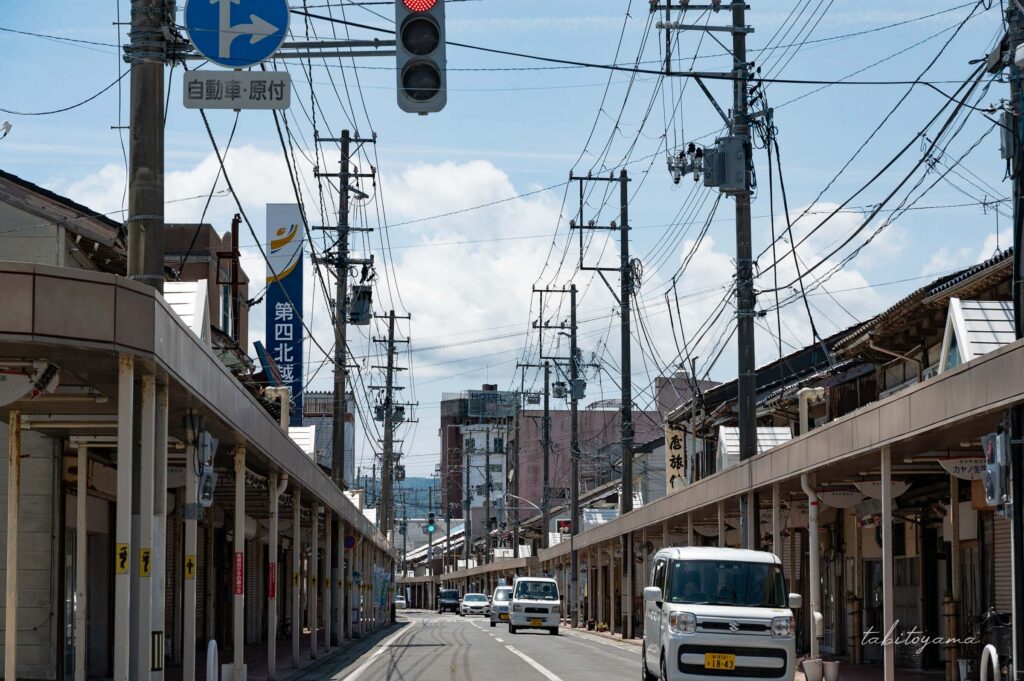 両津港の街中を走る道路、両脇の建物の隙間から青空と白い雲が見える