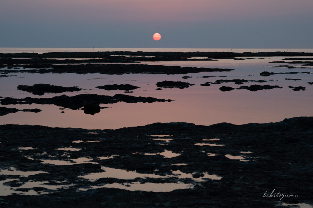 万畳敷の夕日、水平線近くに丸い太陽と手前の海には空のグラデーションが反射している