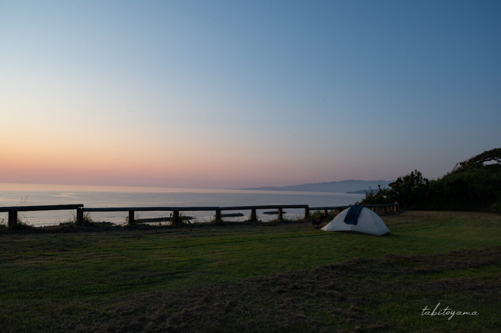 素浜キャンプ場の高台サイトに設営された白いテント、夕焼けに染まる空と水平線が見える