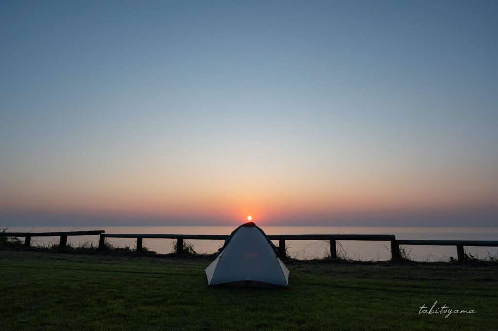 素浜キャンプ場の高台サイト設営された白いテント、天頂部に夕陽が重なり空は夕焼けに染まる