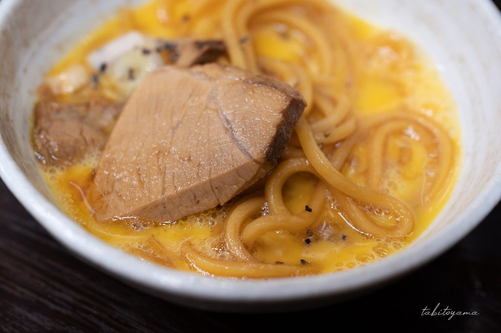 富山ブラックの麺や具材を生卵にくぐらせる