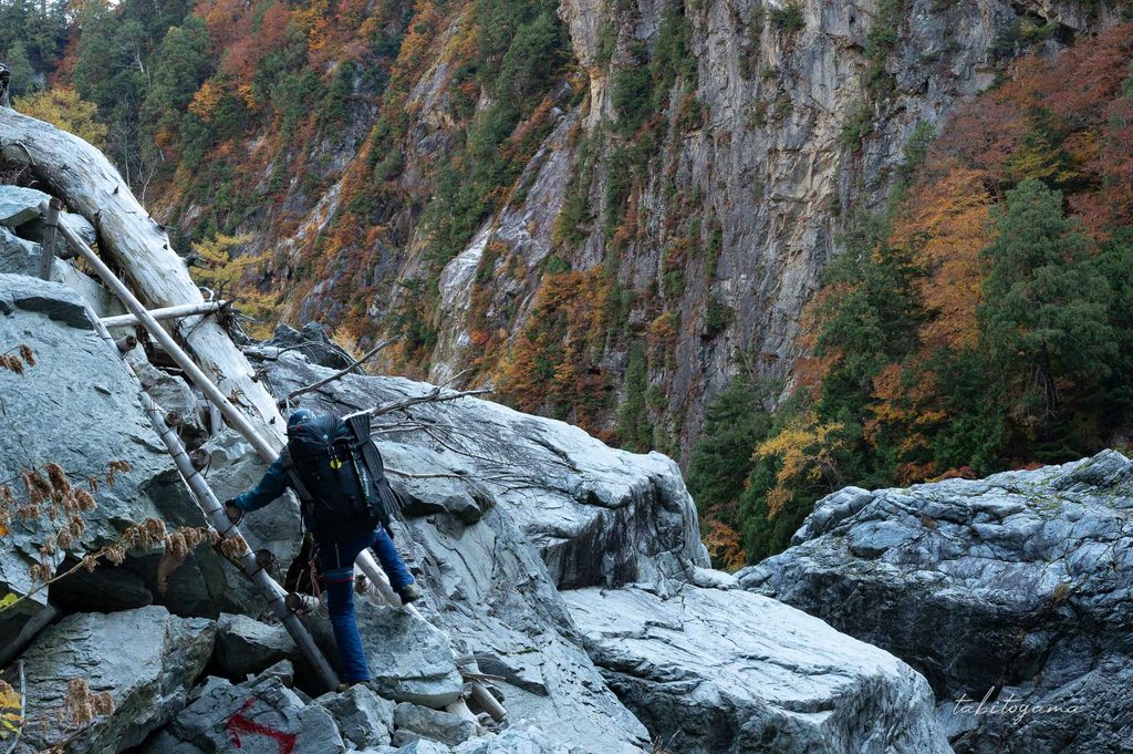 巨大な岸壁を横目にハシゴを登る登山者