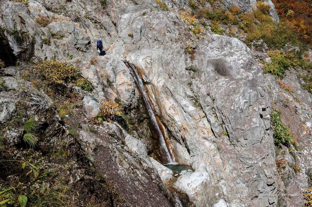 流れ落ちる滝の登山道を歩く人