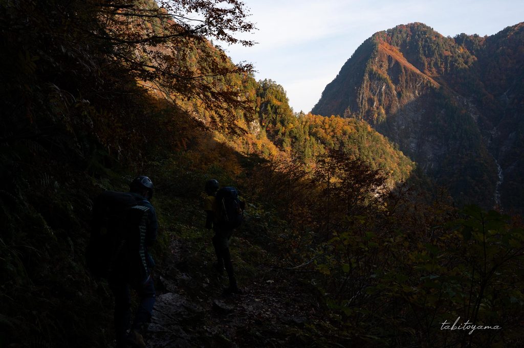日差しが当たらない暗い登山道から視界の先の山々に日差しが当たる様子