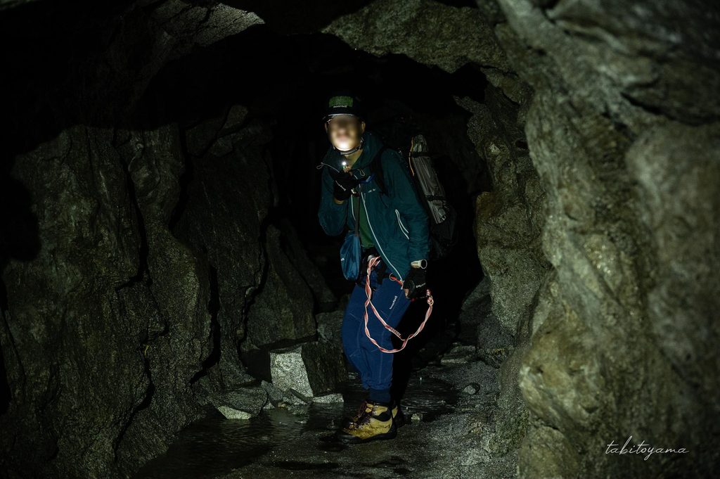 暗いトンネル内部で顔を下部からライトで照らす登山者