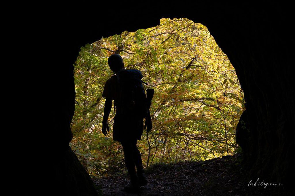 暗いトンネル出口には紅葉が広がりシルエットになる登山者の後ろ姿