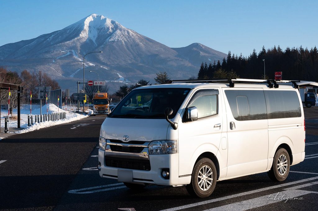 冠雪した磐梯山を背景にサービスエリアに駐車されたハイエース